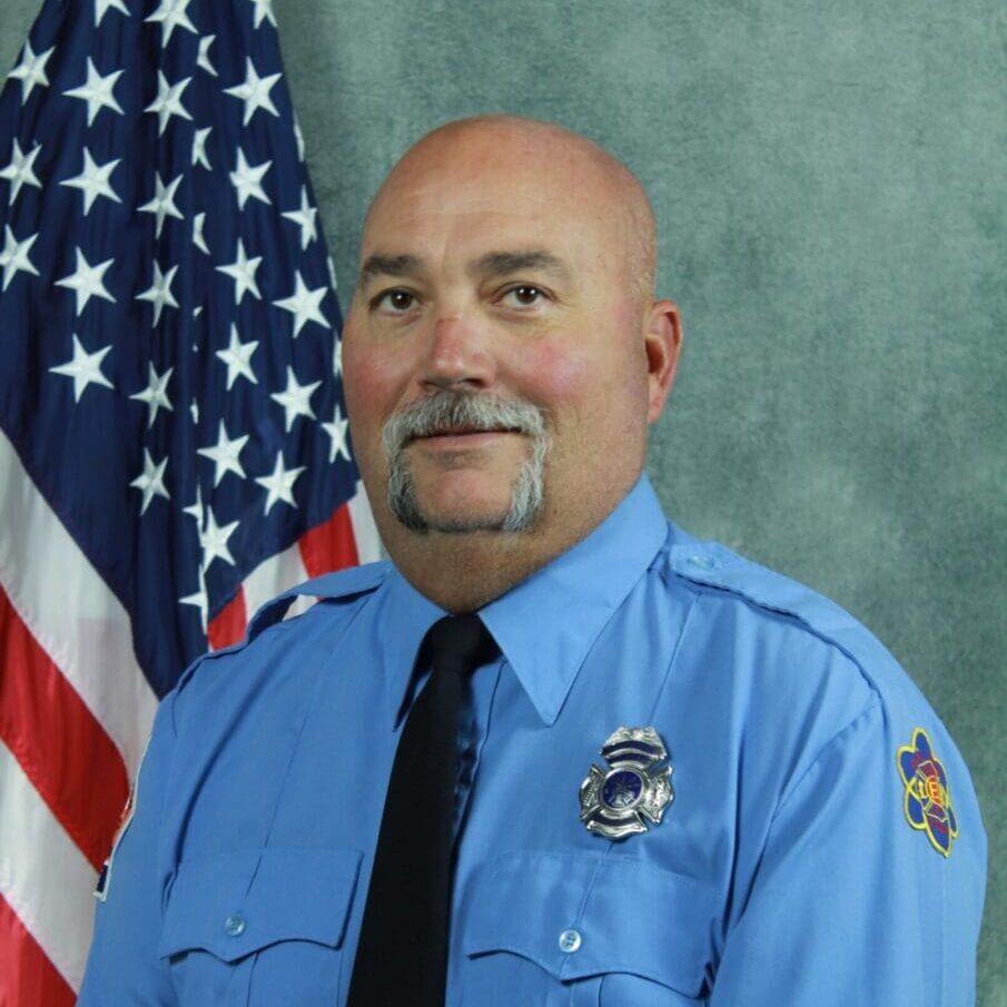 A uniformed fire department officer posing in front of an American flag.