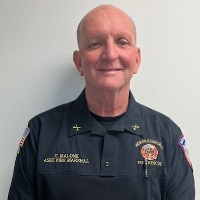 Smiling firefighter in uniform posing against a white wall.