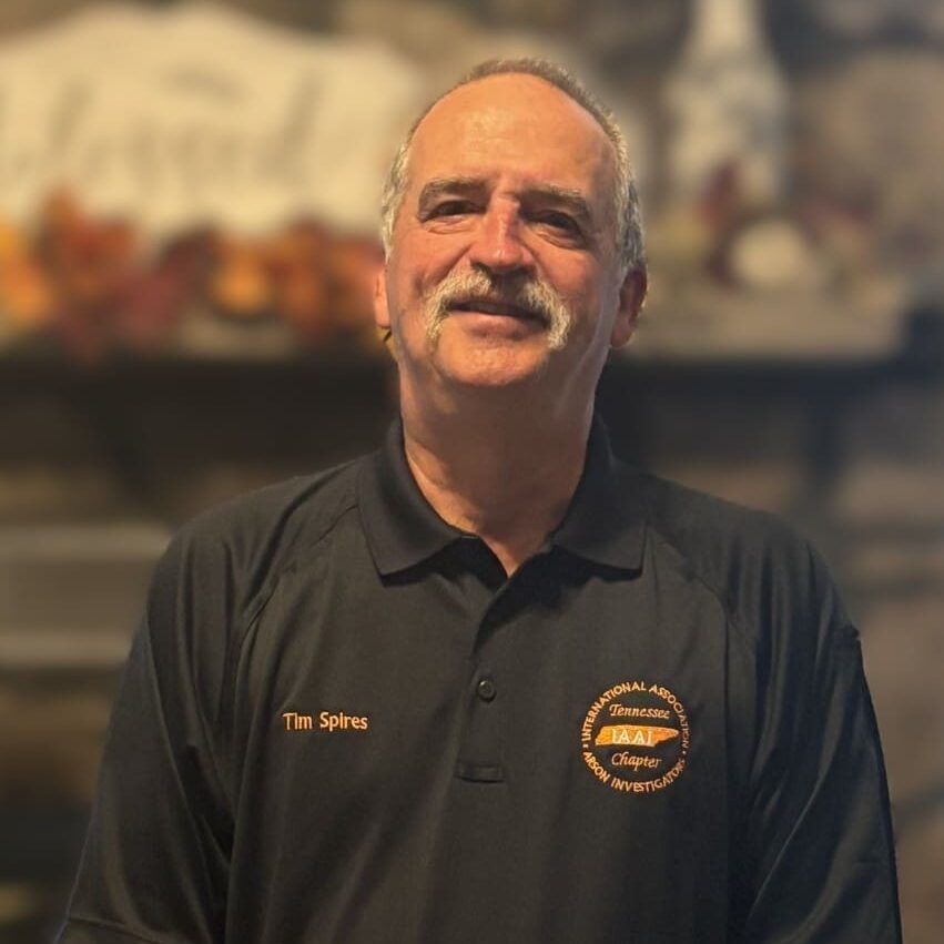 Smiling man in a black polo shirt standing indoors.